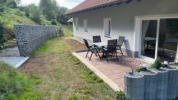 Eine Terrasse mit Tisch und Stühlen, eine Steinmauer und eine Rasenfläche.