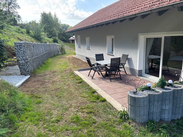A patio with a table and chairs, a stone wall, and a grassy area. - Apartment 'Groß' with Shared Terrace, Shared Garden and Balcony (Waldkirchen)