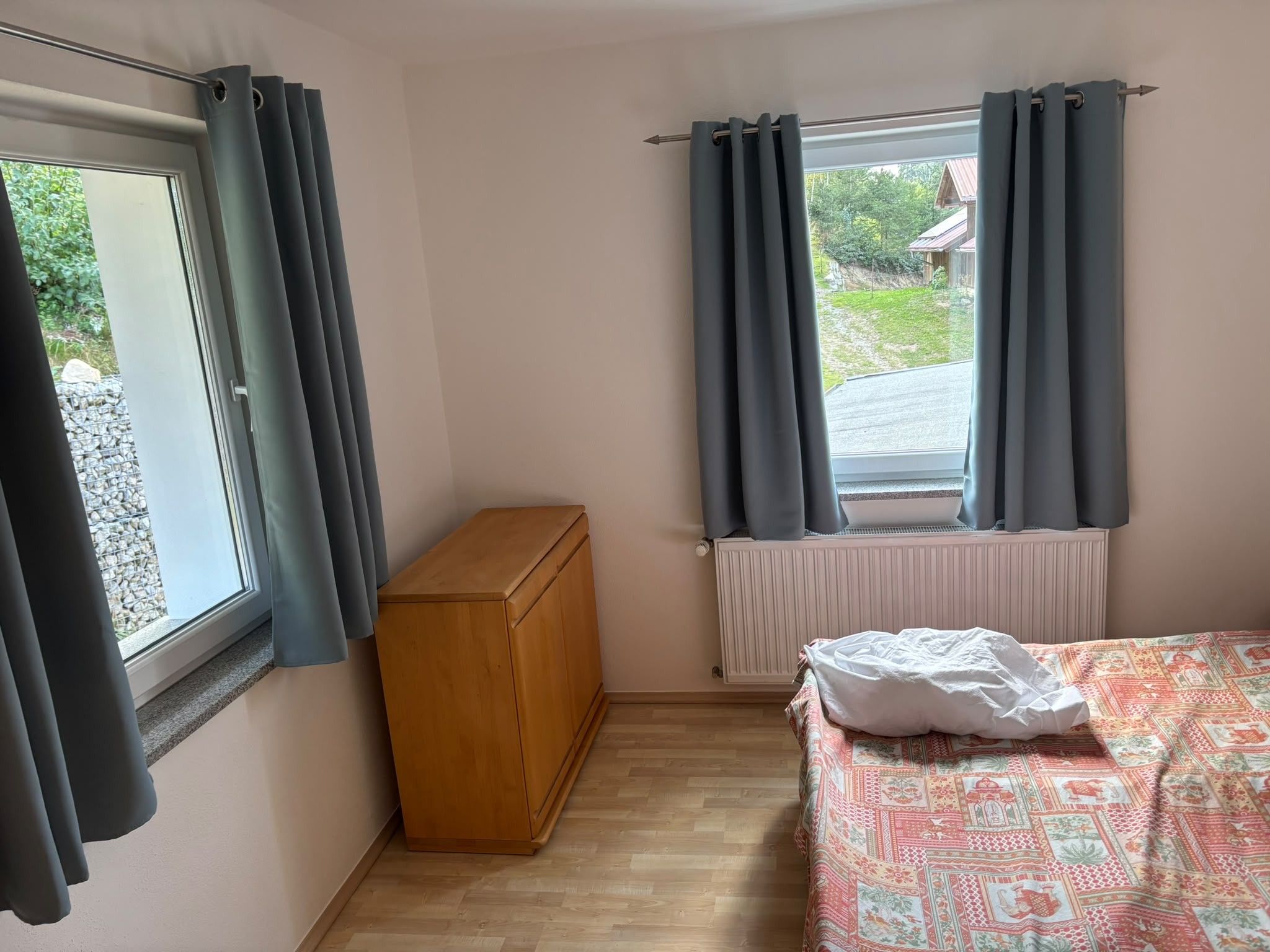 Ein Schlafzimmer mit einem Holzkasten, einem Heizkörper und einem Bett mit einem gemusterten Bettbezug.