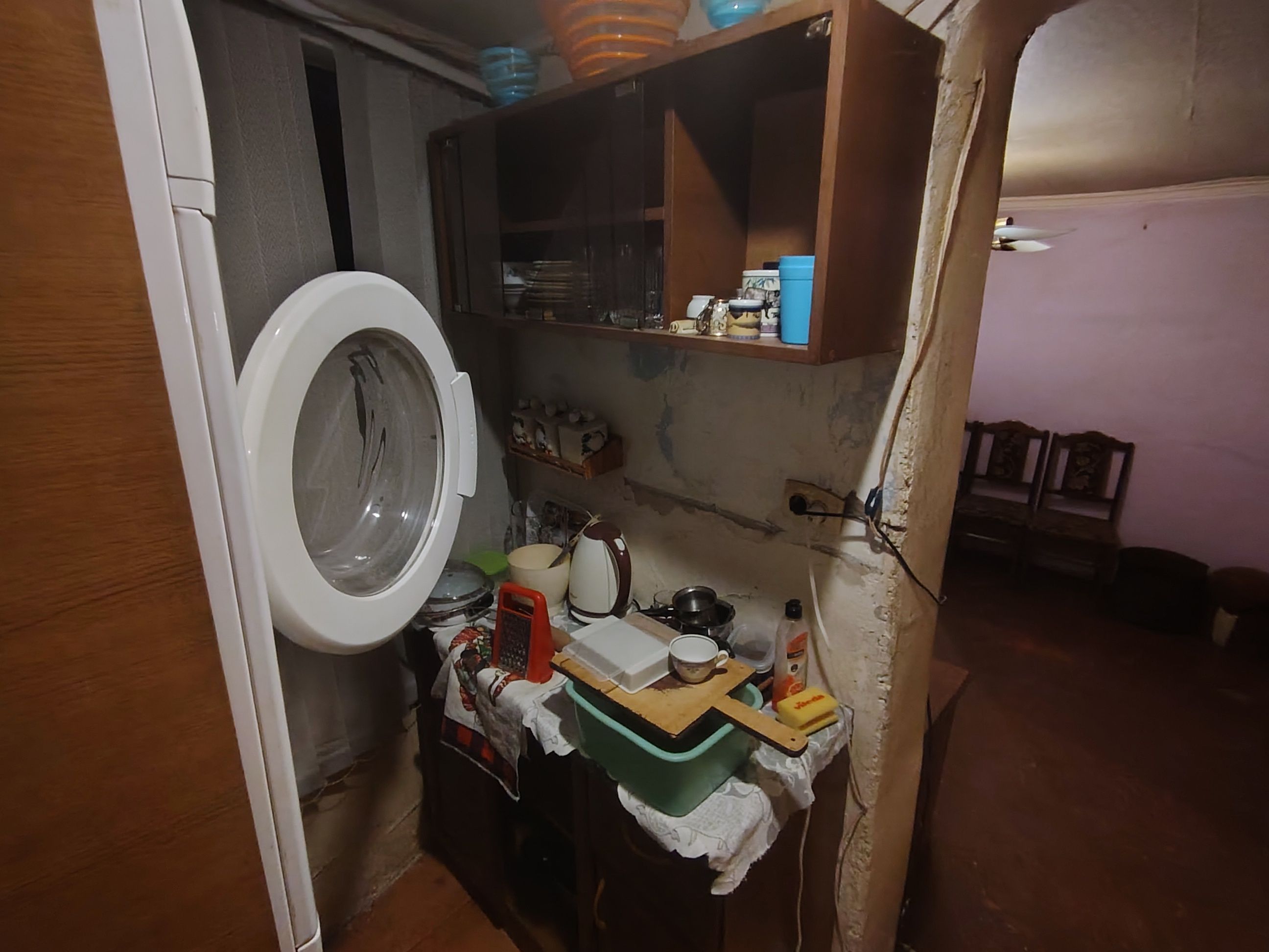 Ein kleines, beengtes Badezimmer mit einer Waschmaschine, einem Regal voller Dinge und einem Holzschrank.