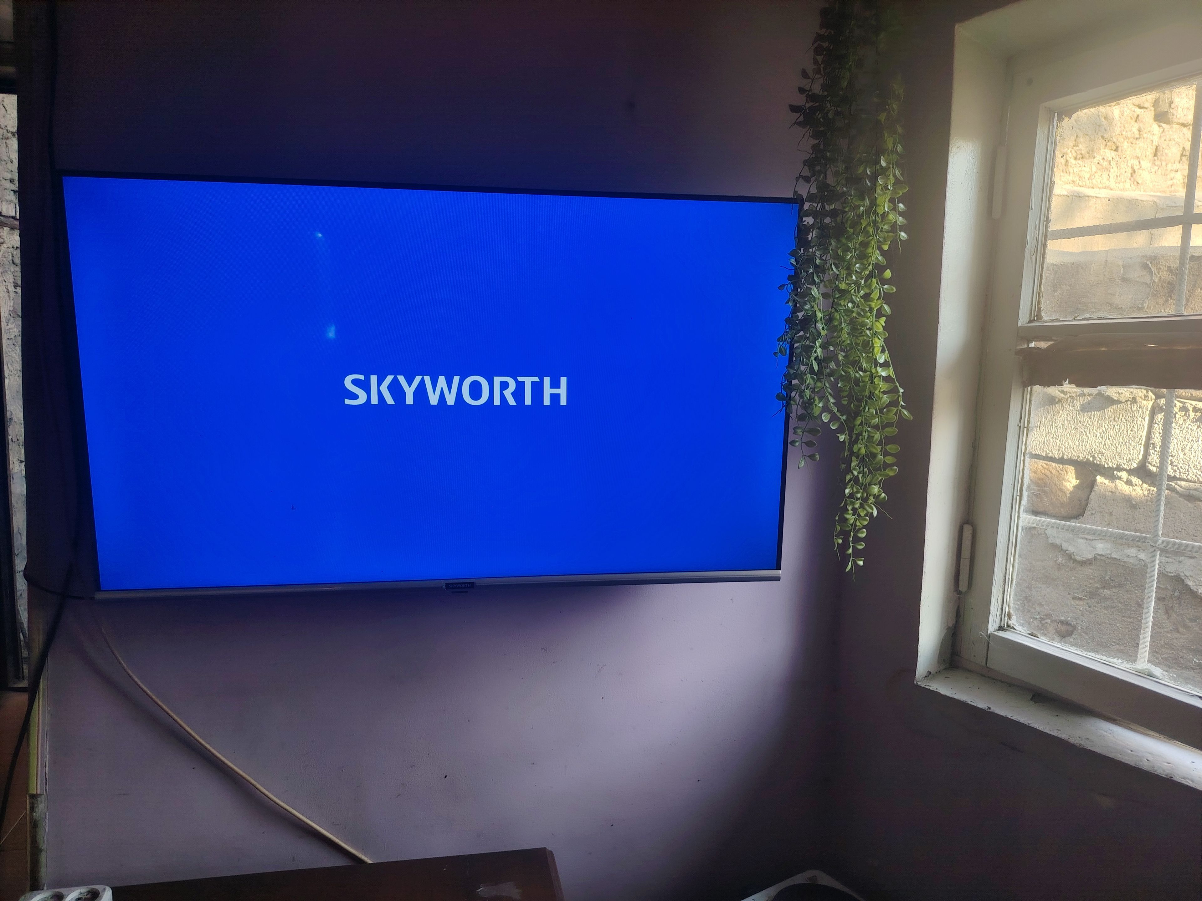 Una TV a schermo piatto montata a parete con la scritta 'SKYWORTH' visualizzata sullo schermo.