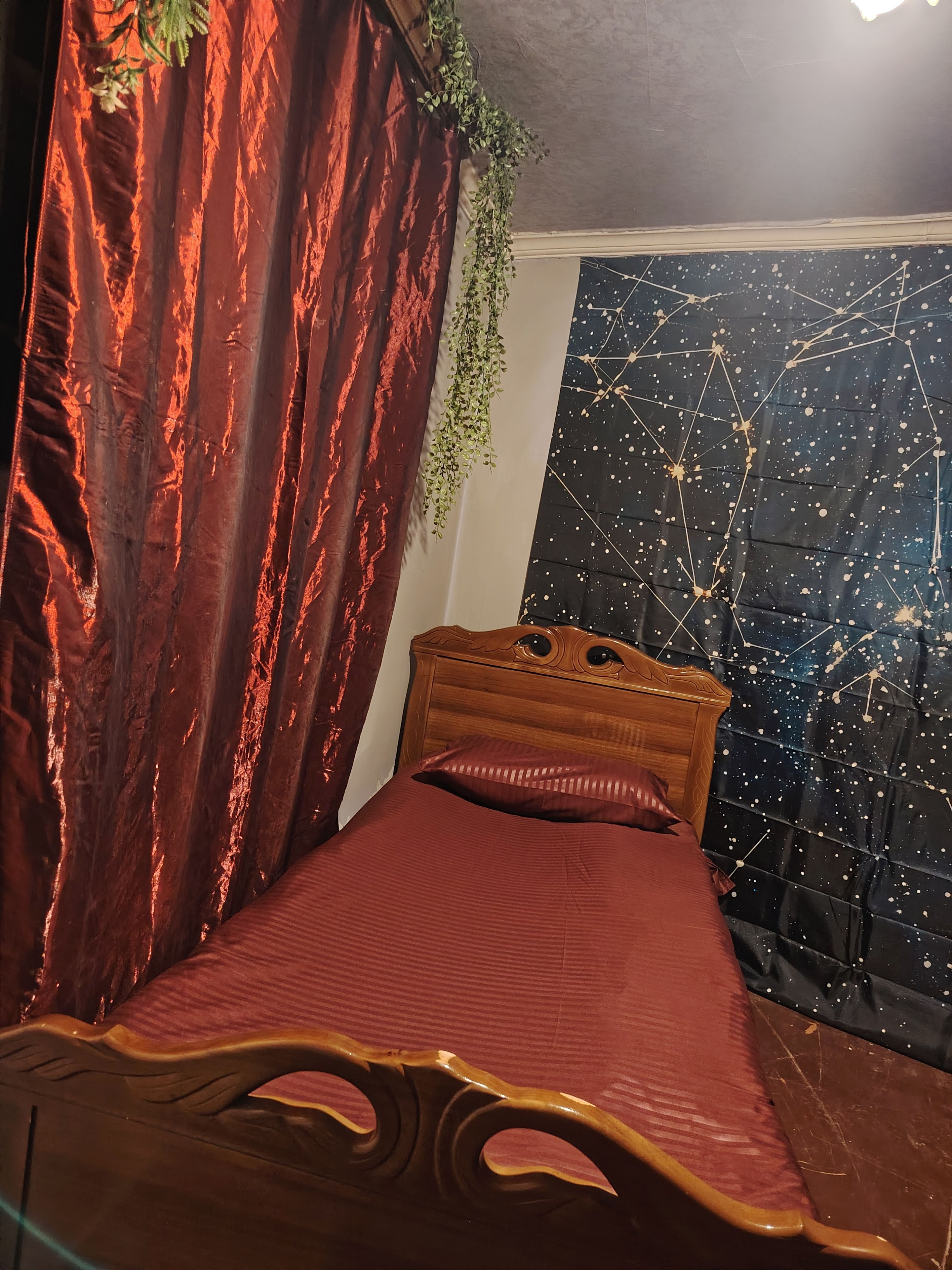 Ein Bett mit Holz-Kopfstück, einer roten Bettdecke und einer Wand mit Sternenmuster.