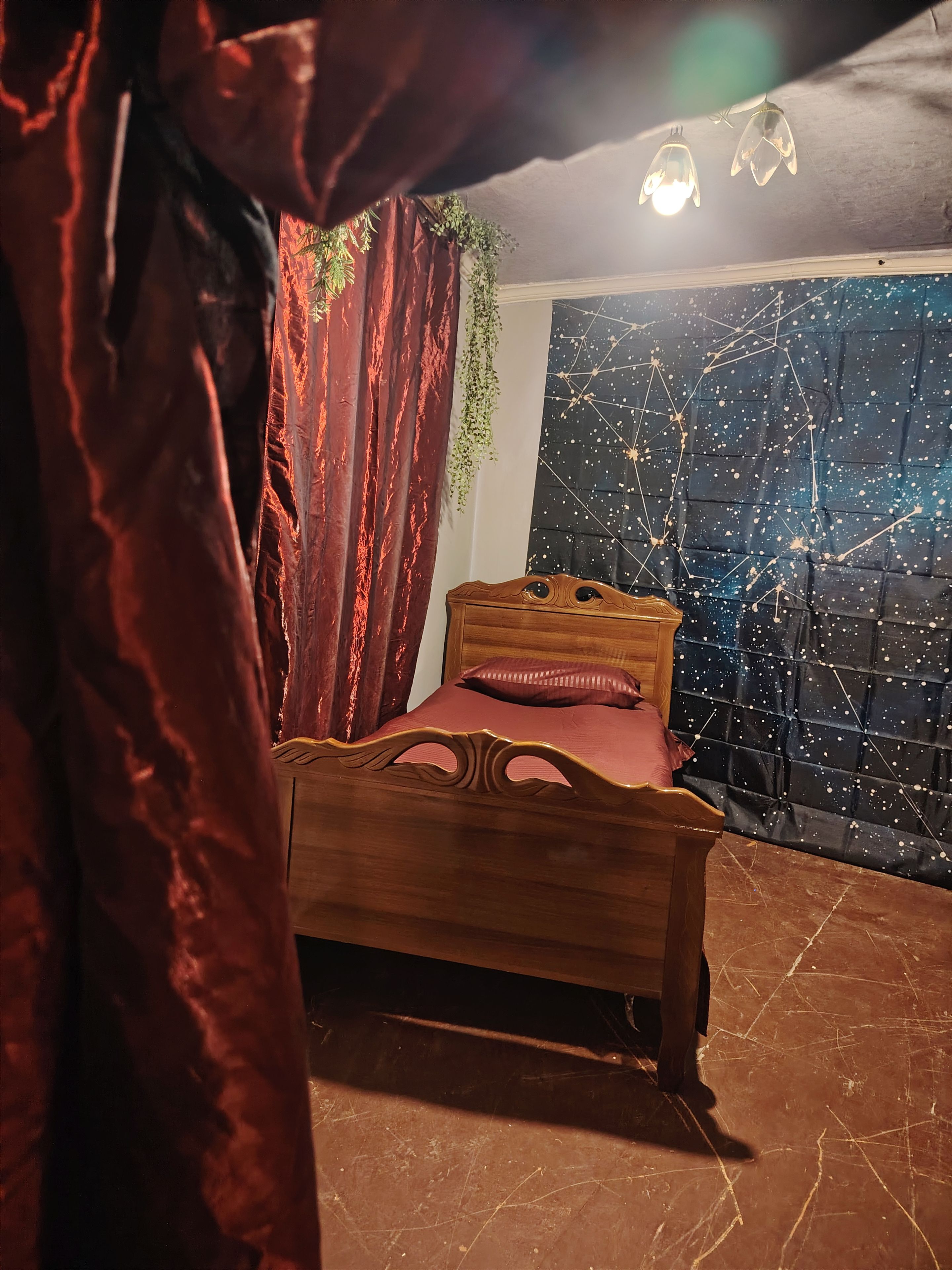 Une chambre avec un lit en bois, des rideaux rouges et un mur orné d’un motif étoilé.