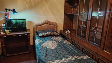 A bedroom with a bed, a wooden cabinet, a desk with a lamp, and a fish tank.