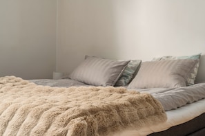 A bed with a fluffy beige blanket, two pillows, and a plain wall. - Arctic Riverside Retreat – Private Sauna - Central (Rovaniemi)