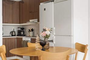 A modern kitchen with wooden cabinets, a white refrigerator, a stove, and a dining table with chairs. - Arctic Riverside Retreat – Private Sauna - Central (Rovaniemi)