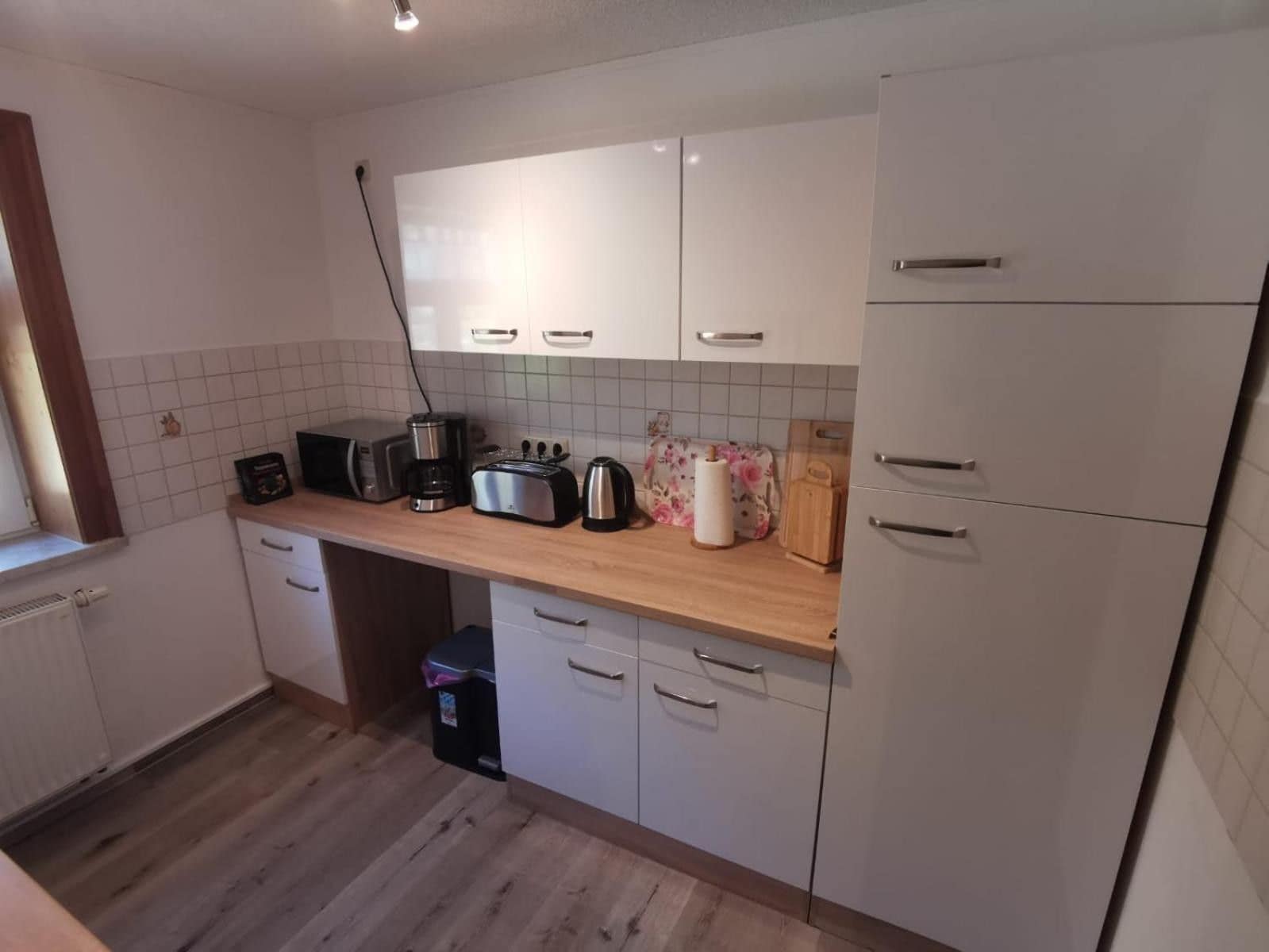 A compact kitchen with white cabinets, a wooden countertop, and basic appliances including a toaster, kettle, and coffee maker.