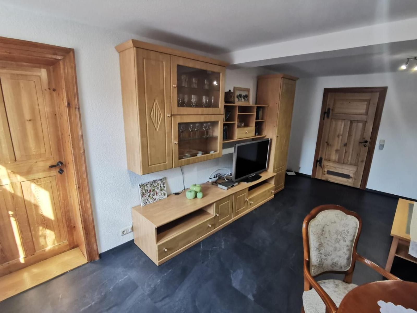 A room with a wooden cabinet with glass doors, a flat-screen TV, and a chair.