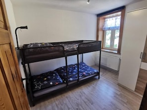 Un llit superposat amb un matalàs estampat de estrelles en una habitació amb terra de fusta, una finestra amb cortina i un radiador.