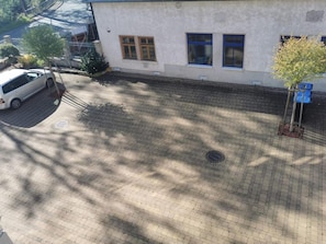 Un patio empedrado con un edificio blanco, un árbol y un coche estacionado.