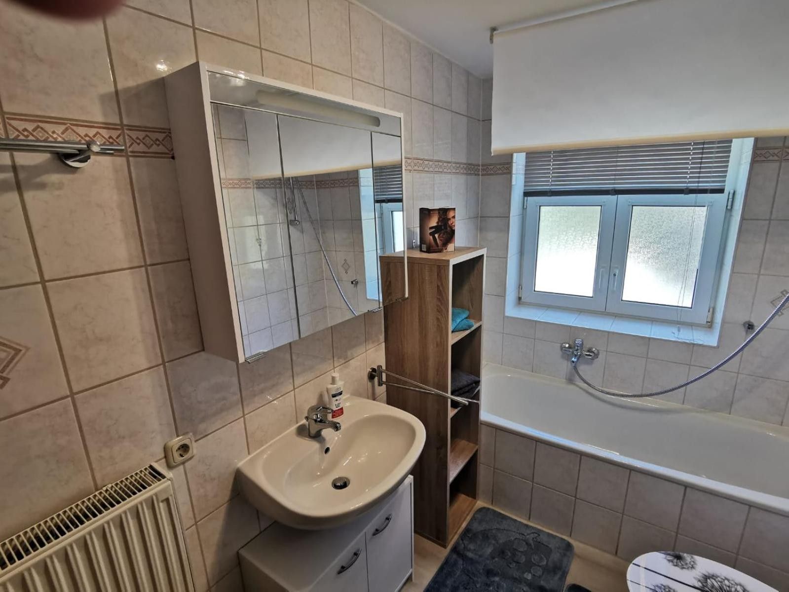 A bathroom with a sink, mirror, shower, and window.