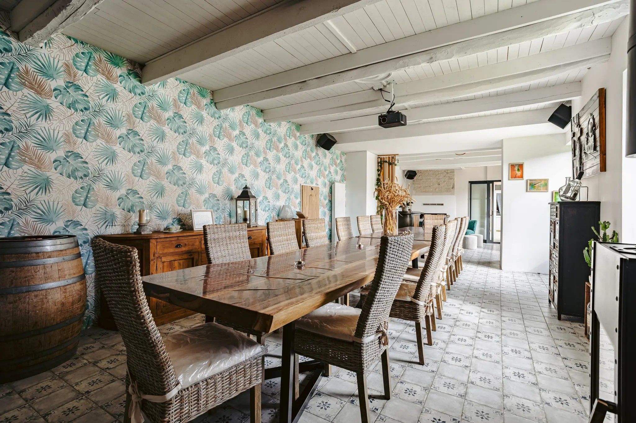 Een eetgedeelte met een lange houten tafel, rieten stoelen, een bewerkte wand en een rustiek plafond.