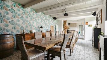Een eetgedeelte met een lange houten tafel, rieten stoelen, een bewerkte wand en een rustiek plafond.