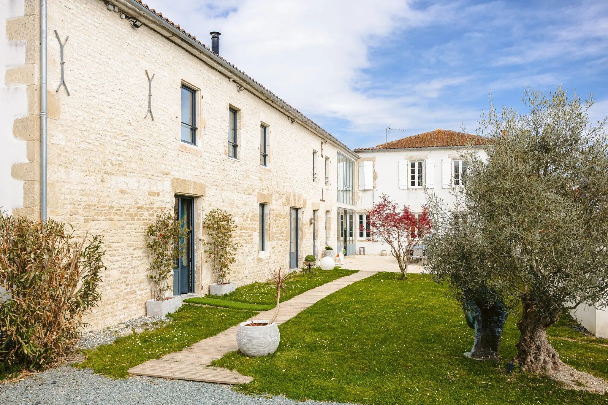 Un bâtiment en pierre doté de nombreuses fenêtres et portes, un chemin pavé et une pelouse bien entretenue agrémentée de diverses plantes.