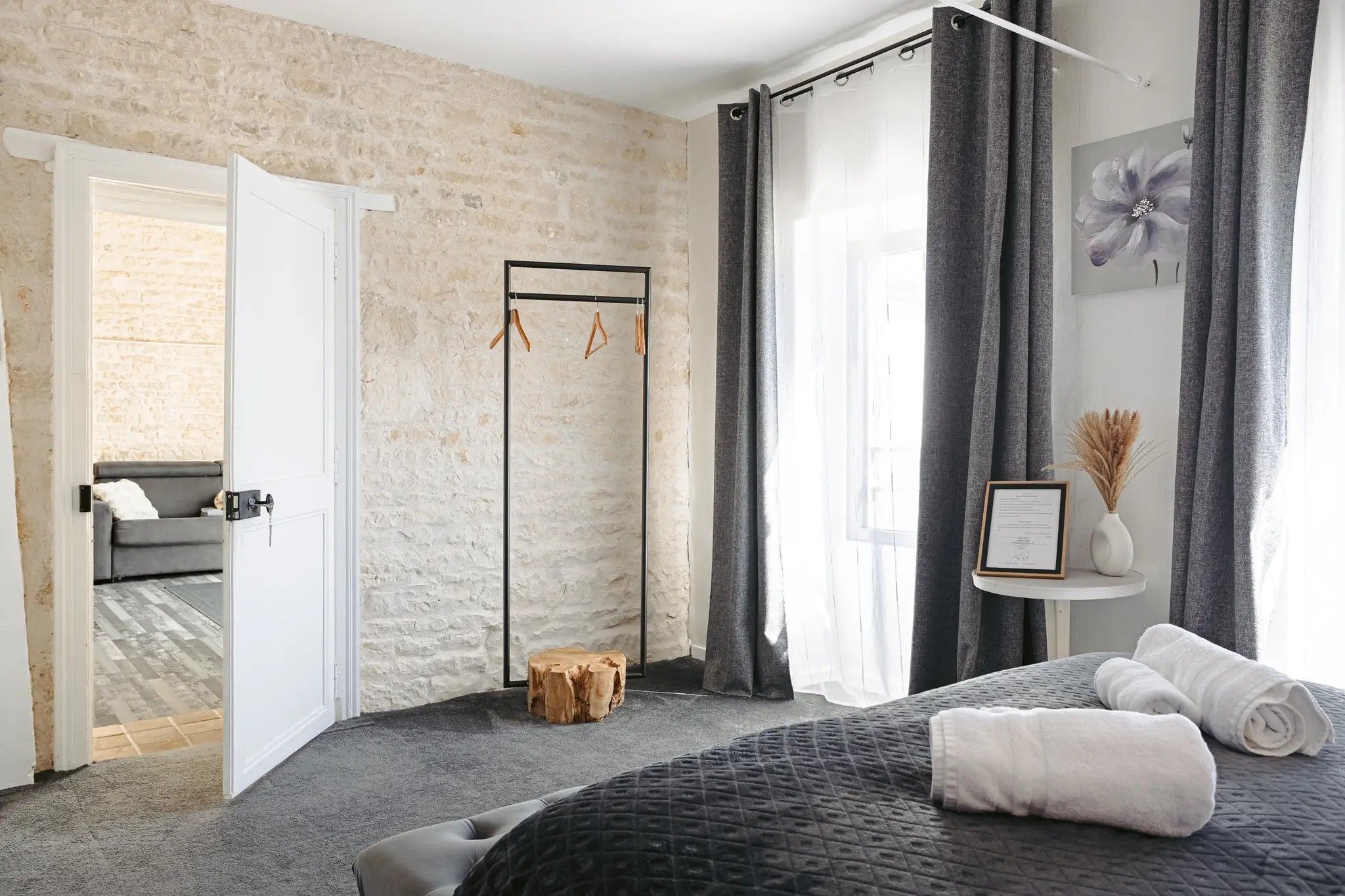 Una camera da letto con un letto, un comodino con un vaso, uno specchio e una porta che dà su un'altra stanza.