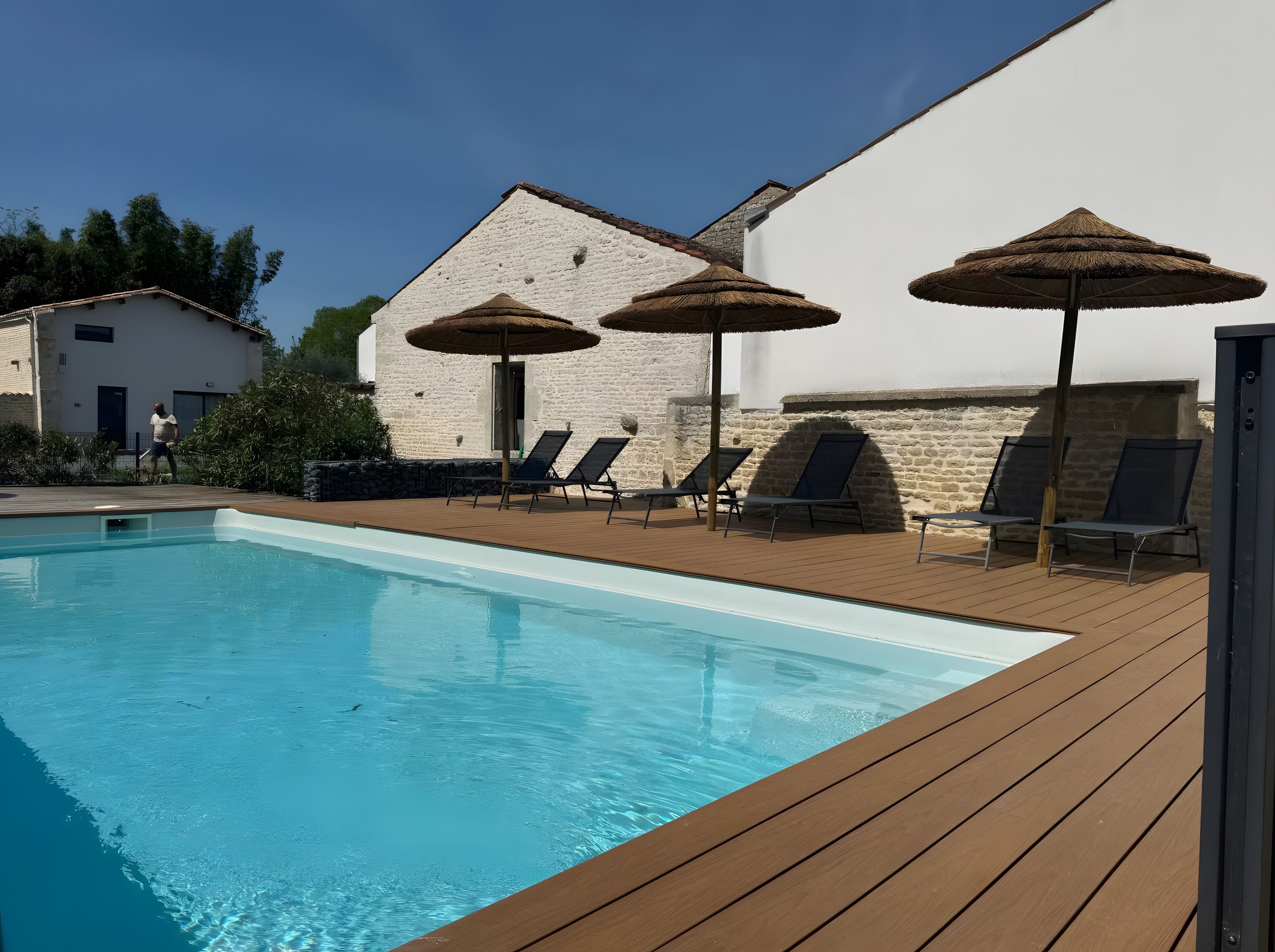 Une piscine entourée de bâtiments en pierre, avec des chaises longues et des parasols.