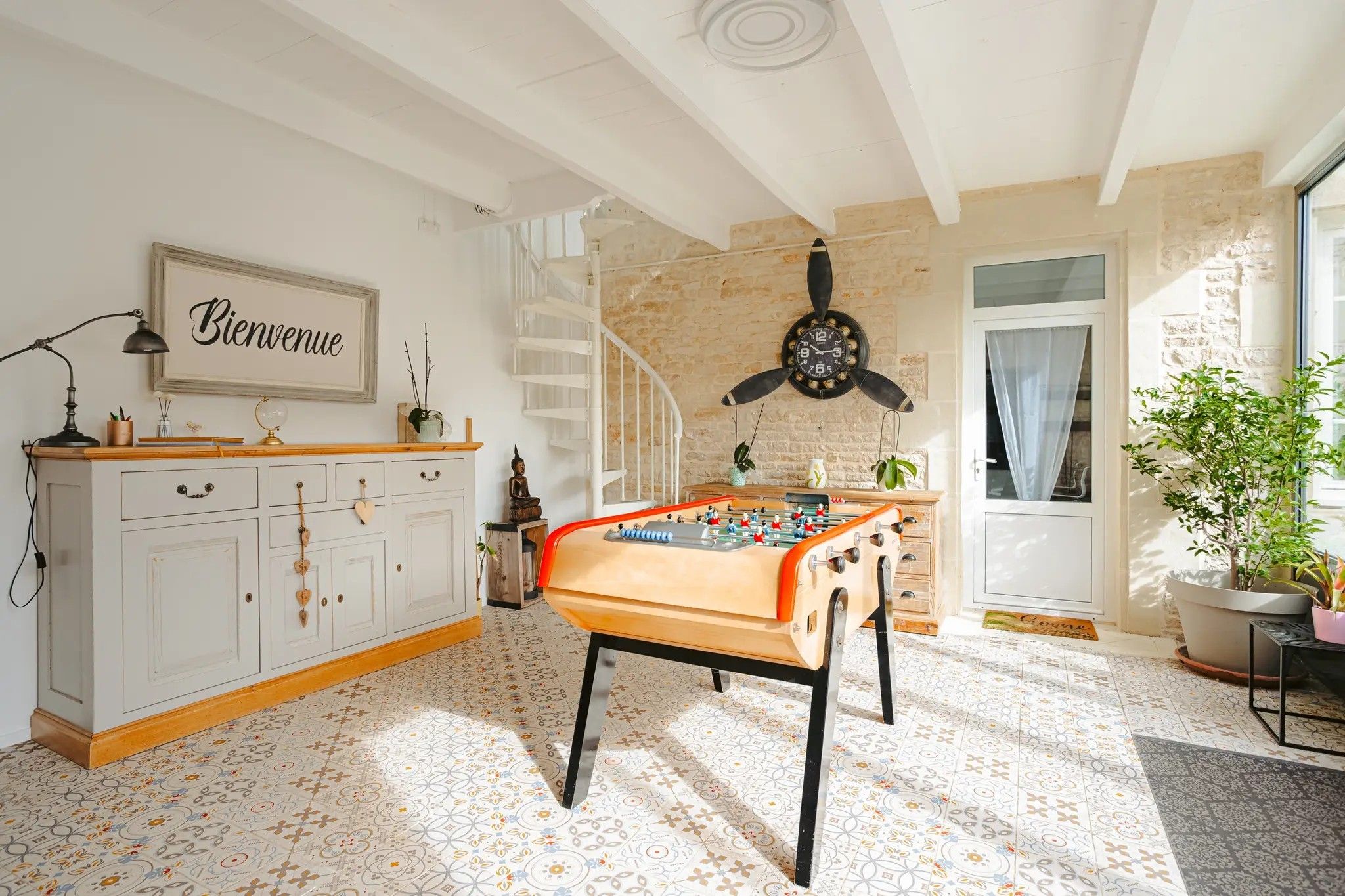 Une pièce avec une table de baby-foot, un escalier et une horloge murale.