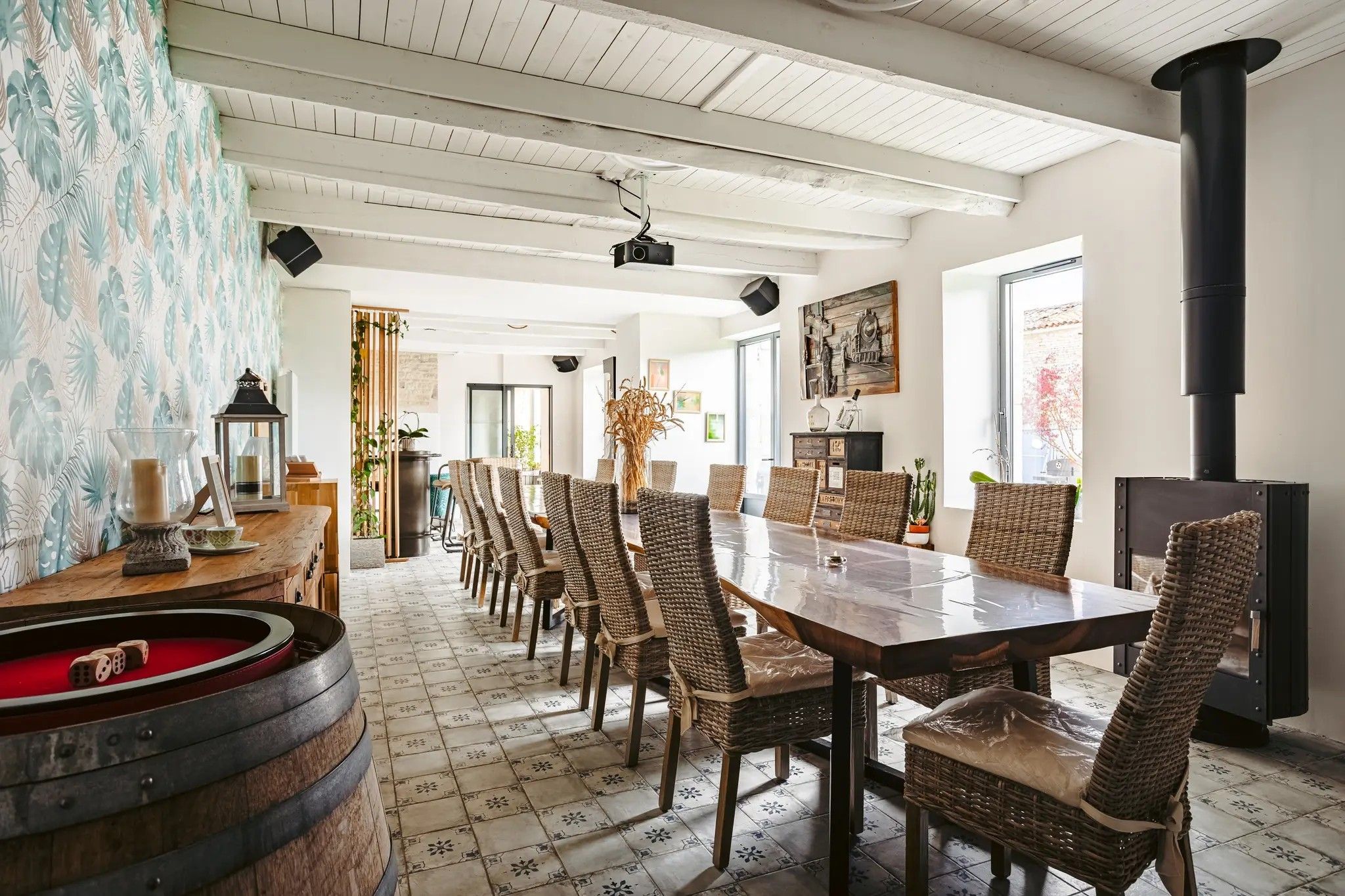 Un espace repas avec une longue table, des chaises en osier et un poêle noir.