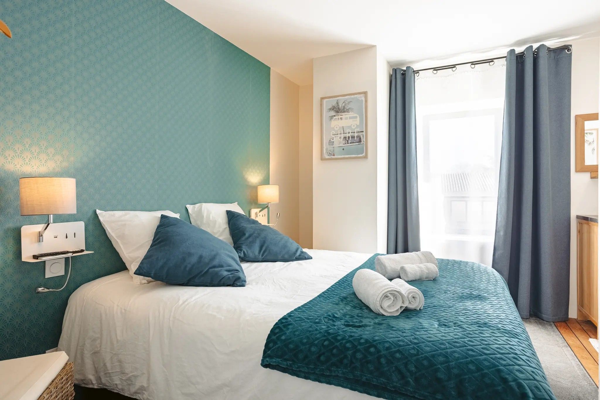 Een hotelkamer met een bed, twee bedlampen, een raam met gordijnen en een aan de muur hangend schilderij.