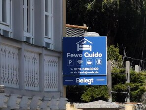 A blue signboard for 'Fewo Quido' with contact information and a bed icon, indicating a hotel or lodging service.