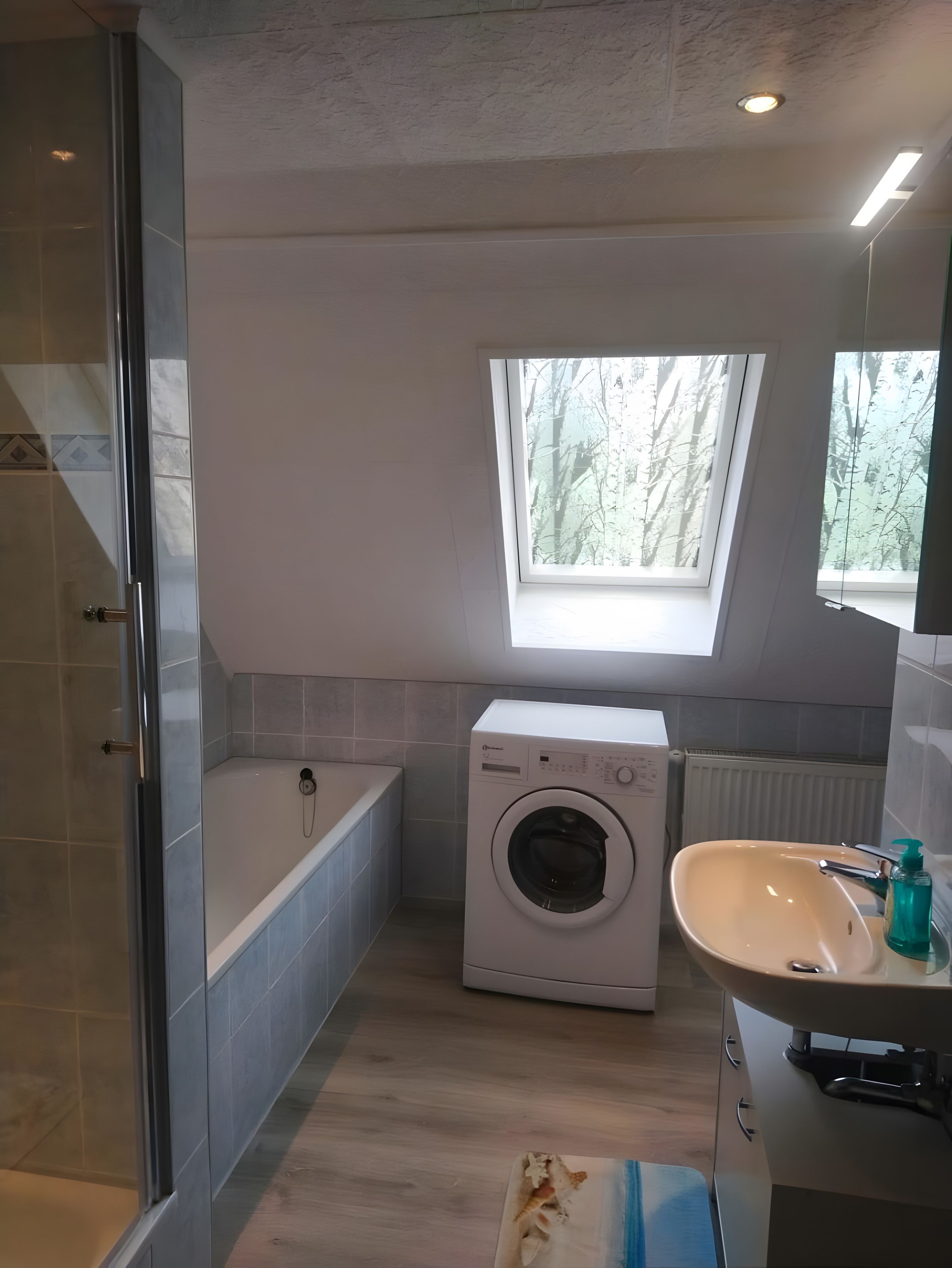 A compact bathroom with a built-in washing machine, a bathtub, and a window providing natural light.