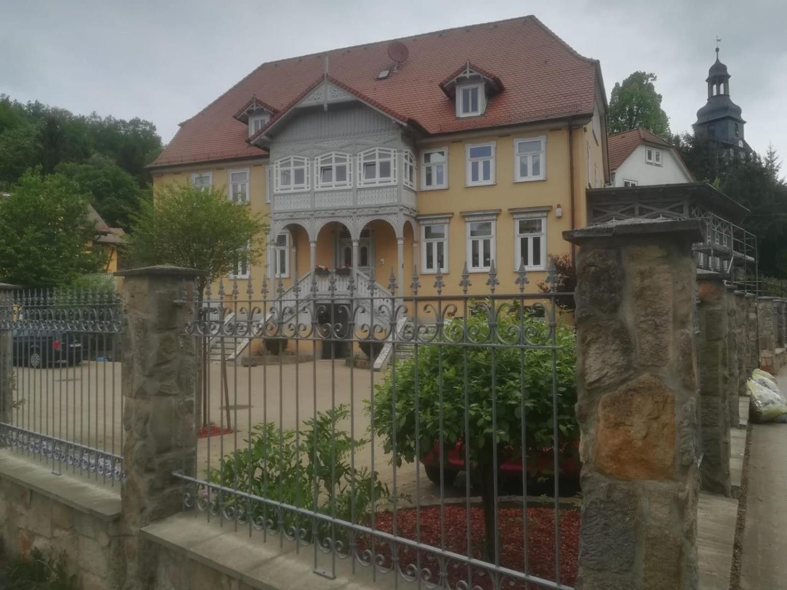 Ein zweistöckiges Gebäude mit rotem Ziegeldach, einem Balkon und einem Steinzaun.