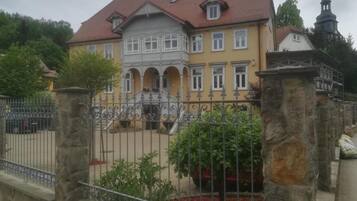 Ein zweistöckiges Gebäude mit rotem Ziegeldach, einem Balkon und einem Steinzaun.