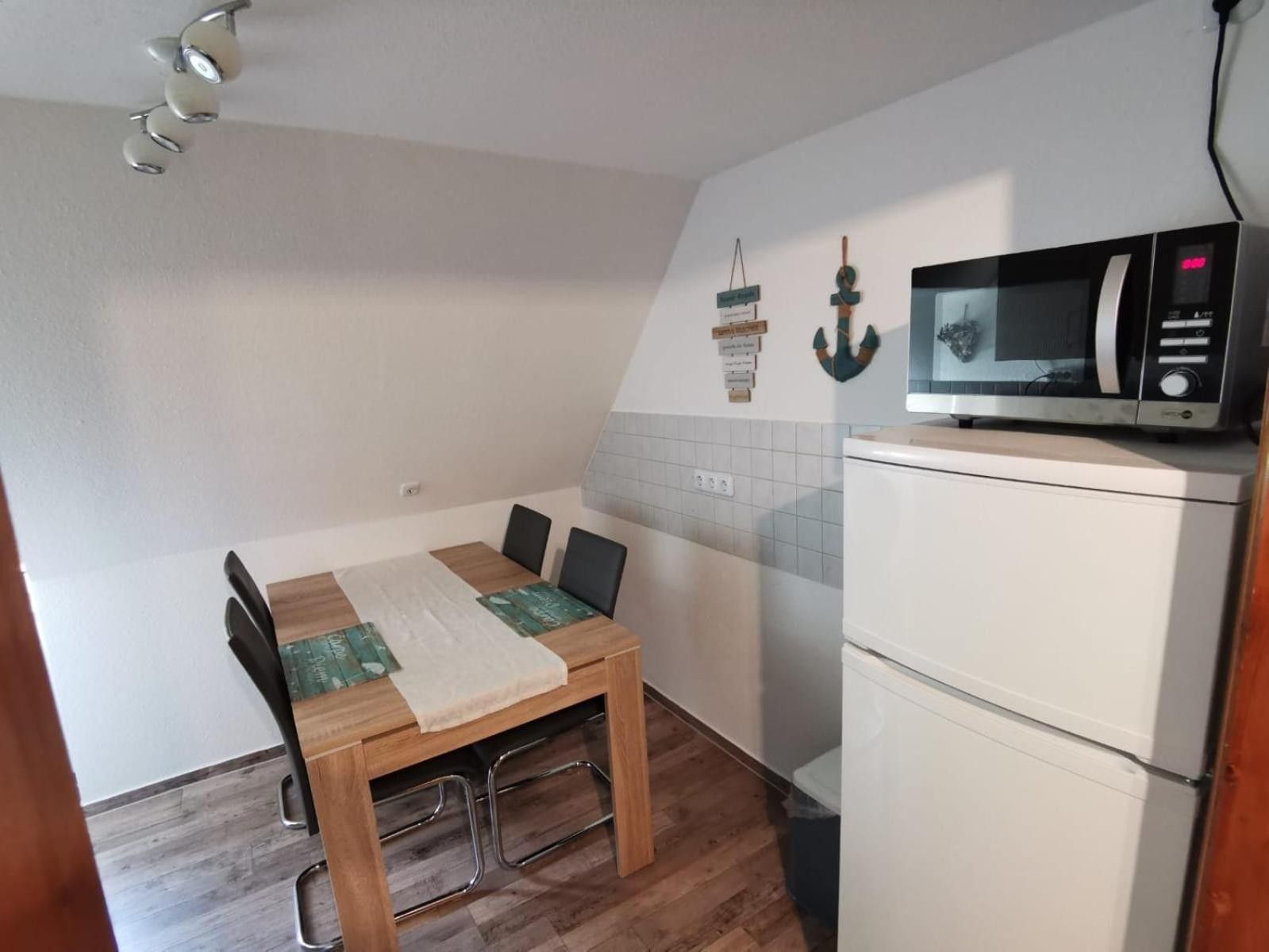 A compact kitchen with a dining table, chairs, a microwave, and a refrigerator.