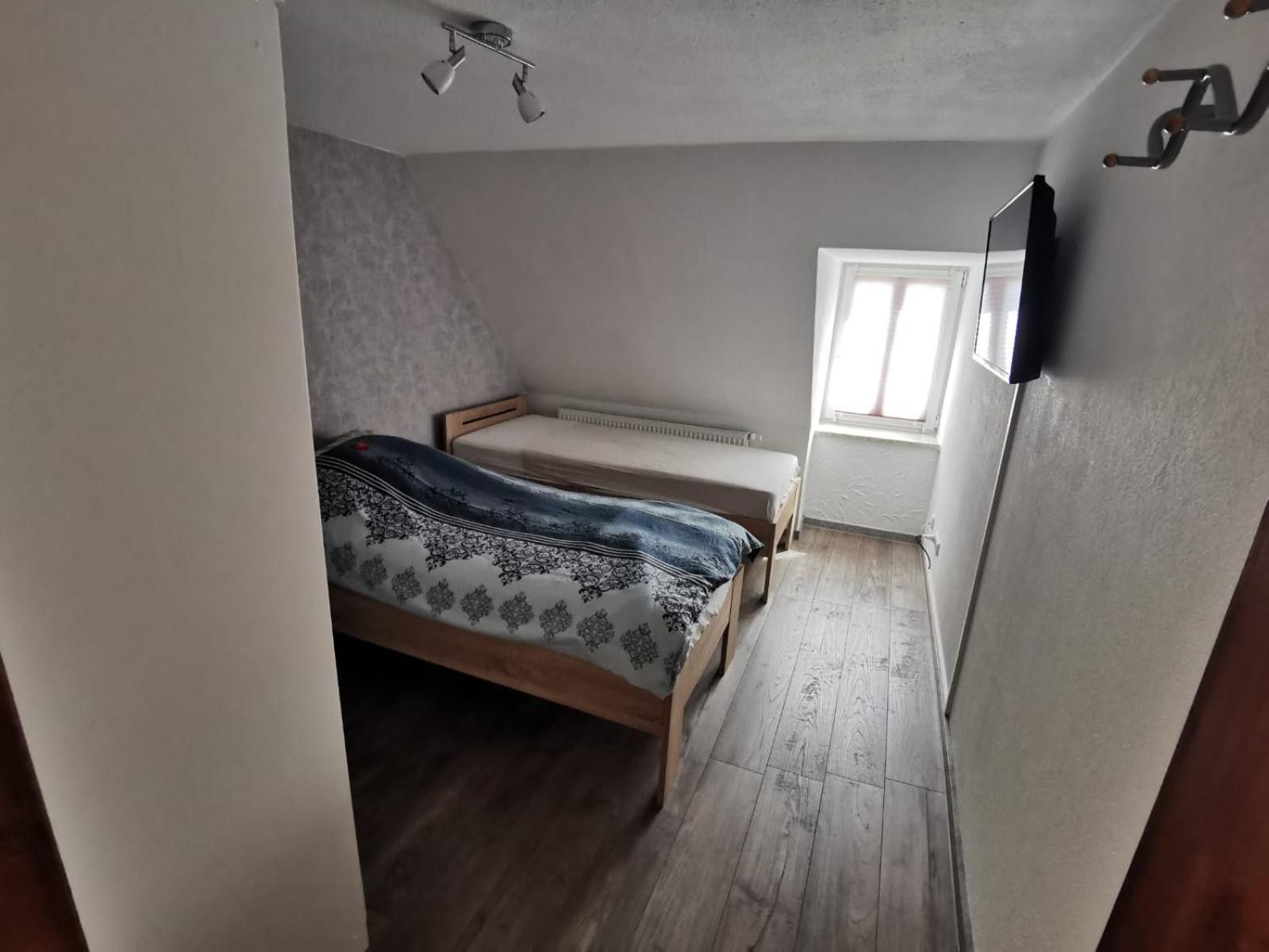 Ein kleines Zimmer mit einem Einzelbett, geneigter Decke, Heizkörper und einem Fenster mit Jalousien.