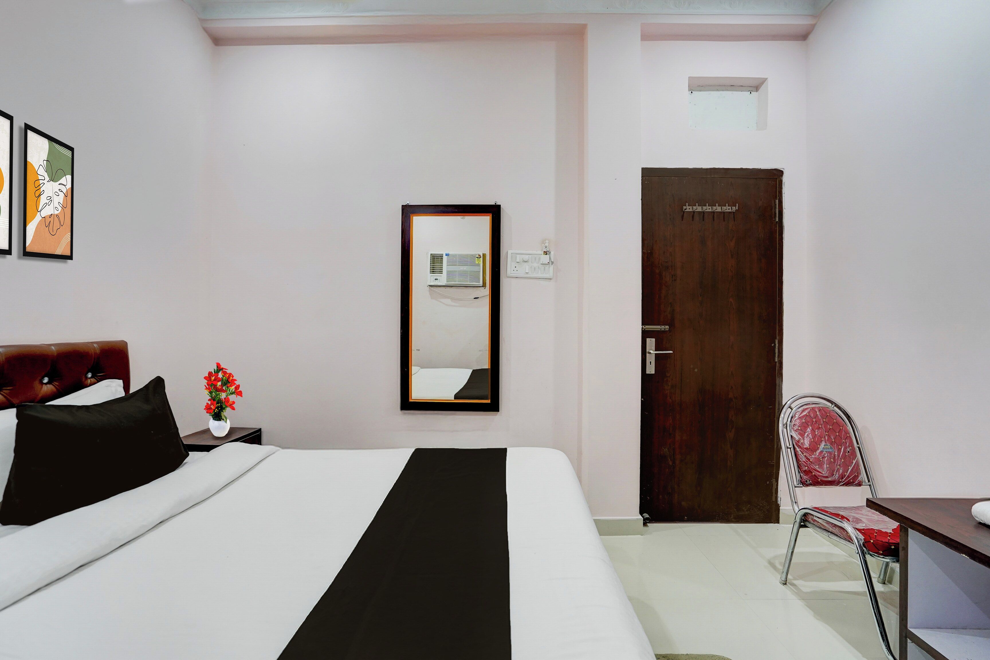 A hotel room with a bed, a desk, a chair, a door, and a mirror on the wall.