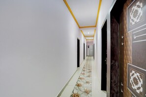 A hallway with a patterned floor, white walls, and a wooden door with a geometric design. - Super Collection O Patna Airport (Danapur)