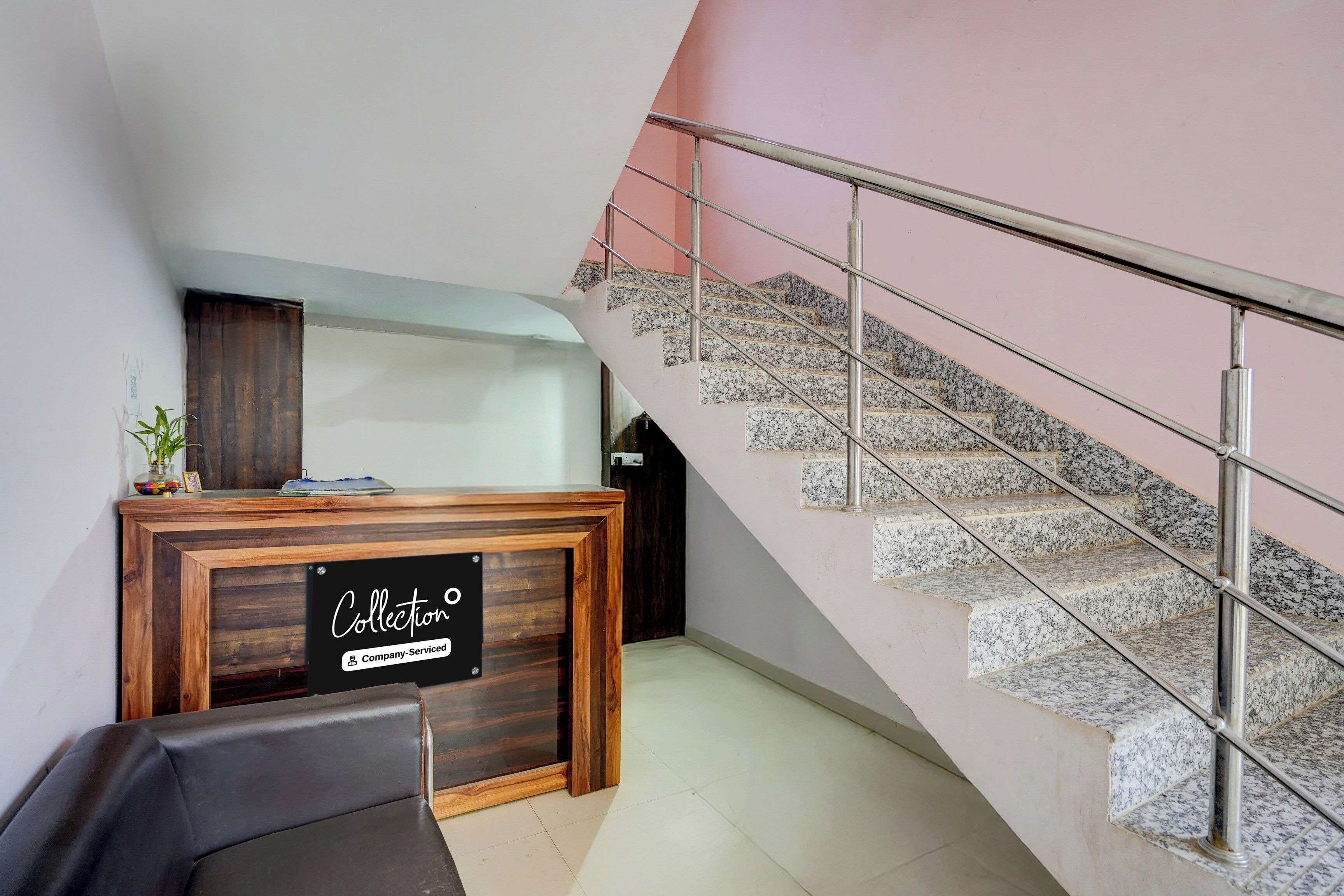 A reception desk with a sign indicating it is company-serviced, a staircase with metal railings, and a wall with a pink hue.