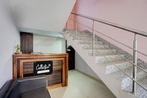 A reception desk with a sign indicating it is company-serviced, a staircase with metal railings, and a wall with a pink hue. - Super Collection O Patna Airport (Danapur)