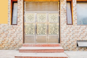 A building entrance with a stone facade, a metal door with intricate patterns, and a set of steps leading up to it. - Hotel O Sector 93 Noida (Noida)