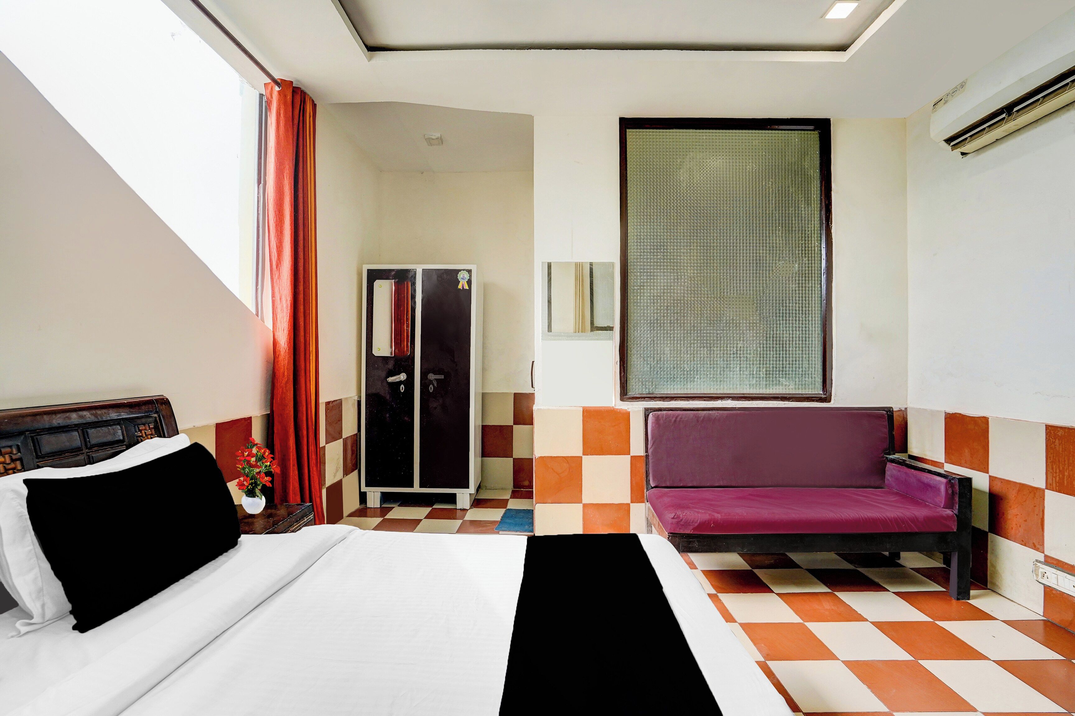 A hotel room with a bed, a sofa, a wardrobe, and a window with blinds.