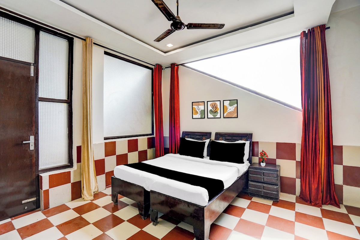 A hotel room with a bed, a ceiling fan, a window with curtains, and a checkered floor.
