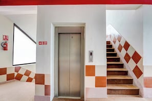 A fire exit sign, an elevator, and a staircase with checkered tiles. - Hotel O Sector 93 Noida (Noida)