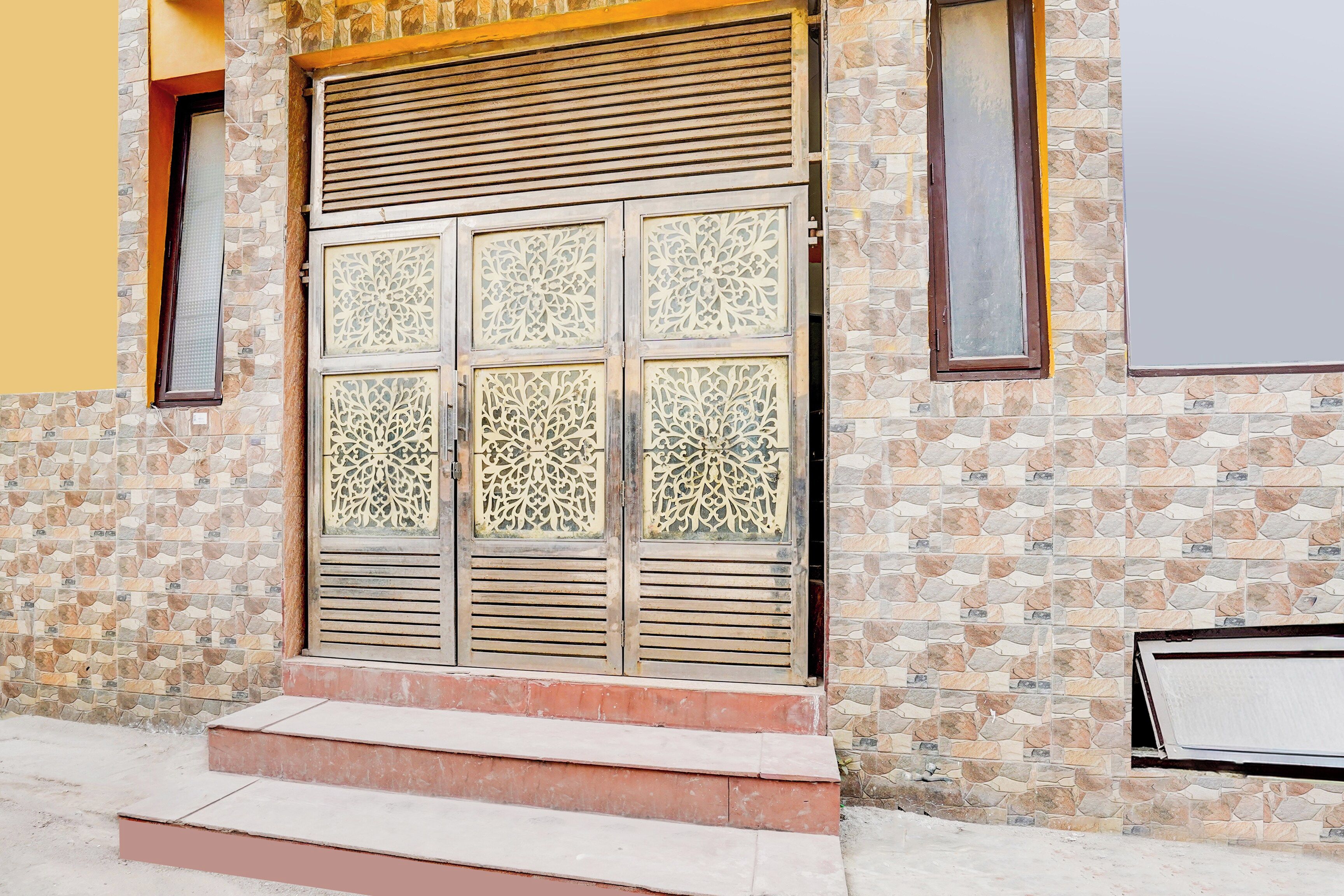 A building entrance with a large decorative door, steps leading up to it, and a stone wall.