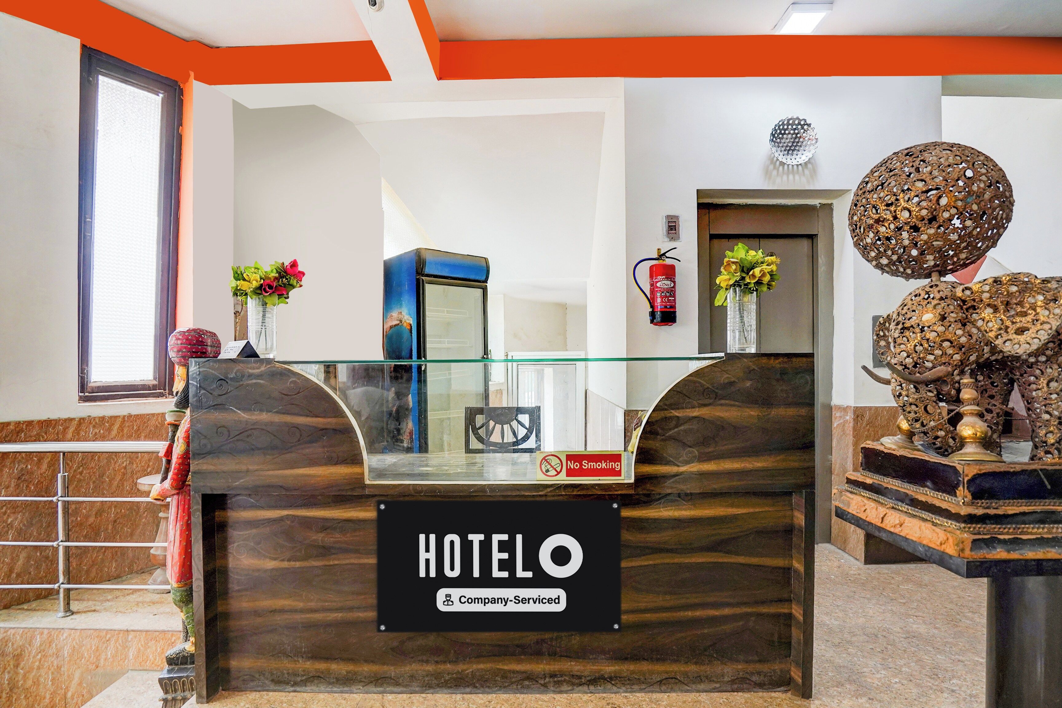 A hotel reception desk with a 'No Smoking' sign, a fire extinguisher, and a 'Company-Serviced' label.