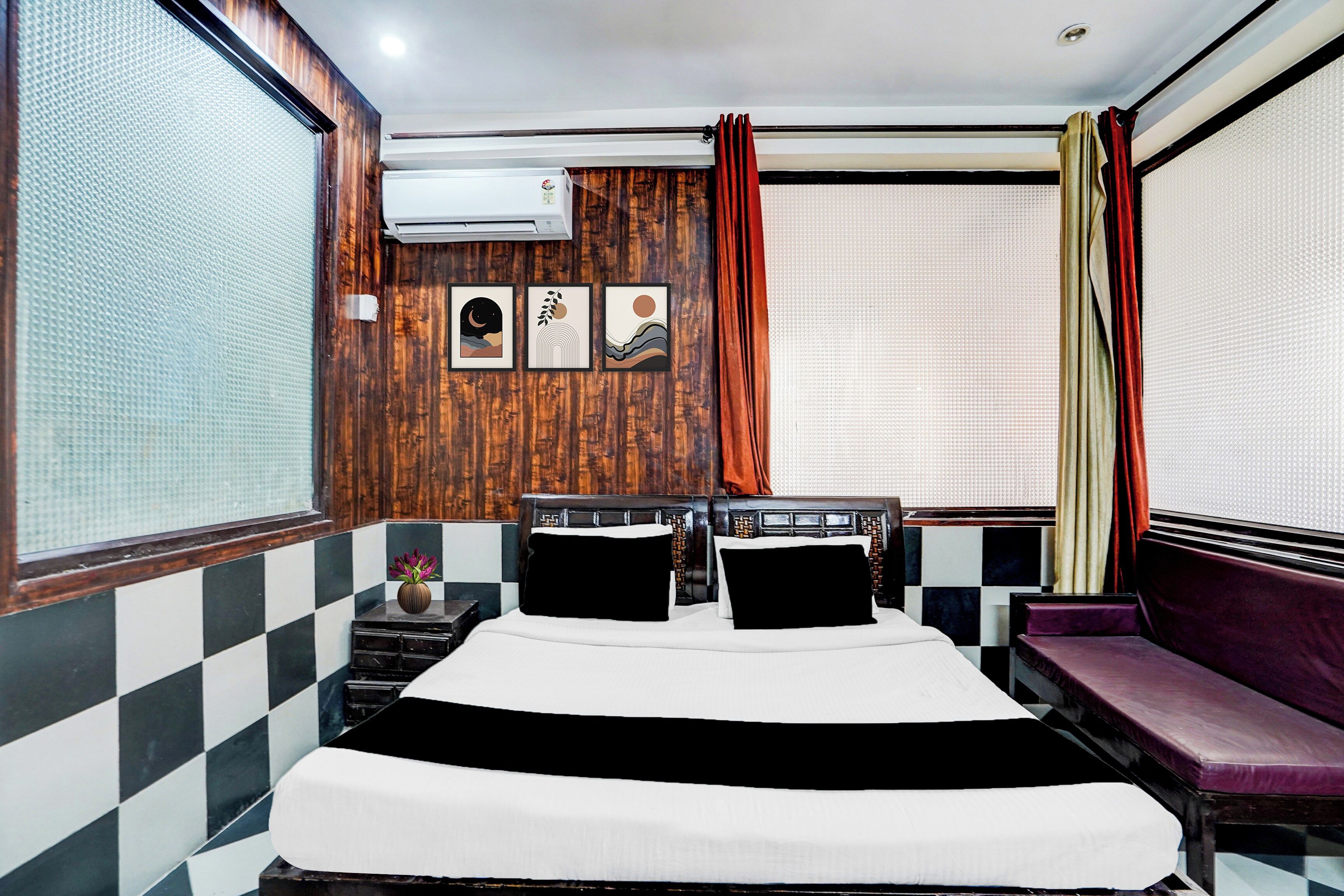 Une chambre d’hôtel comprenant un lit, un coin salon, une fenêtre avec des rideaux et des œuvres d’art accrochées au mur.