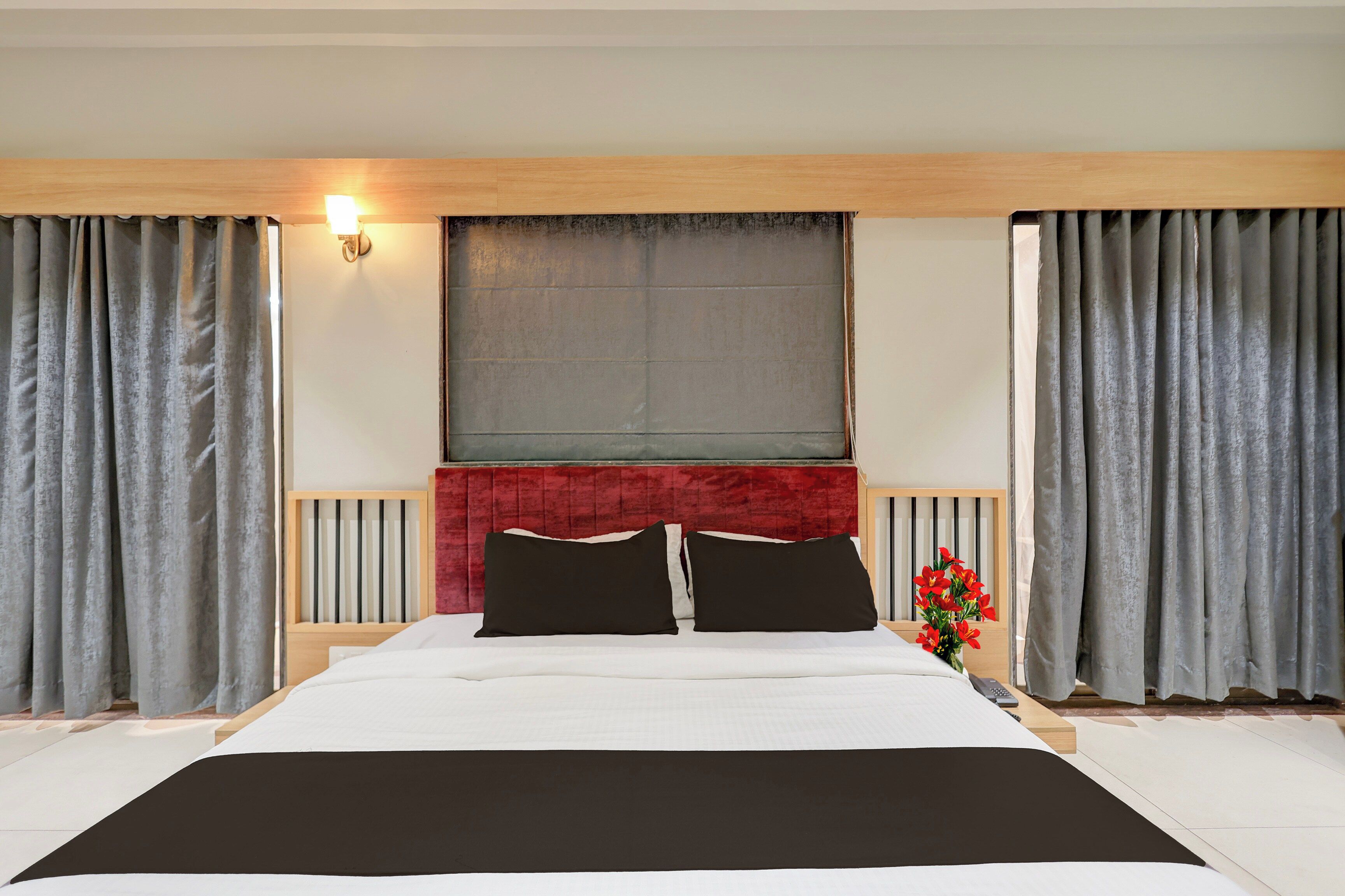 A hotel room with a large bed, a red headboard, grey curtains, and a window with a view.