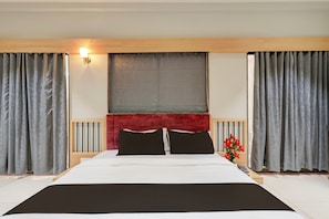A hotel room with a large bed, a red headboard, grey curtains, and a window with a view.