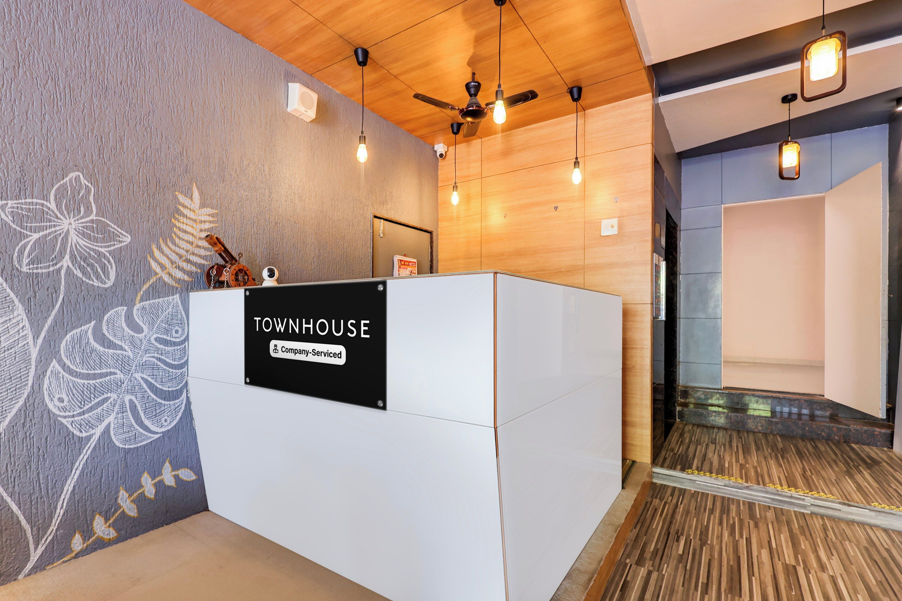 A reception desk with a sign reading 'TOWNHOUSE Company-Serviced' in a modern interior with wooden paneling and a decorative wall.