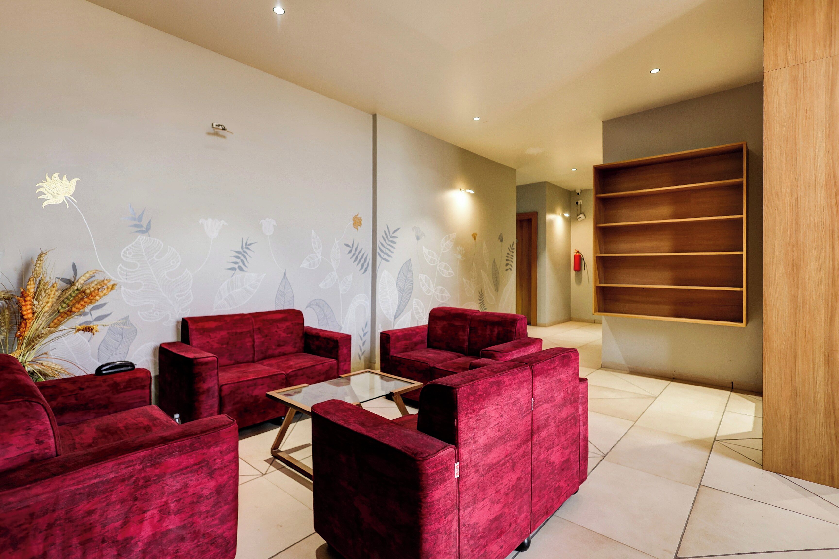 Un espace d’accueil moderne avec des canapés rouges, une table basse en verre et un mur décoratif orné de motifs floraux.