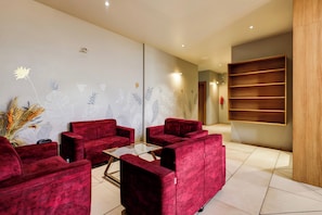 Una moderna zona de recepción con sofás rojos, una mesa de centro de vidrio y una pared decorativa con motivos florales.