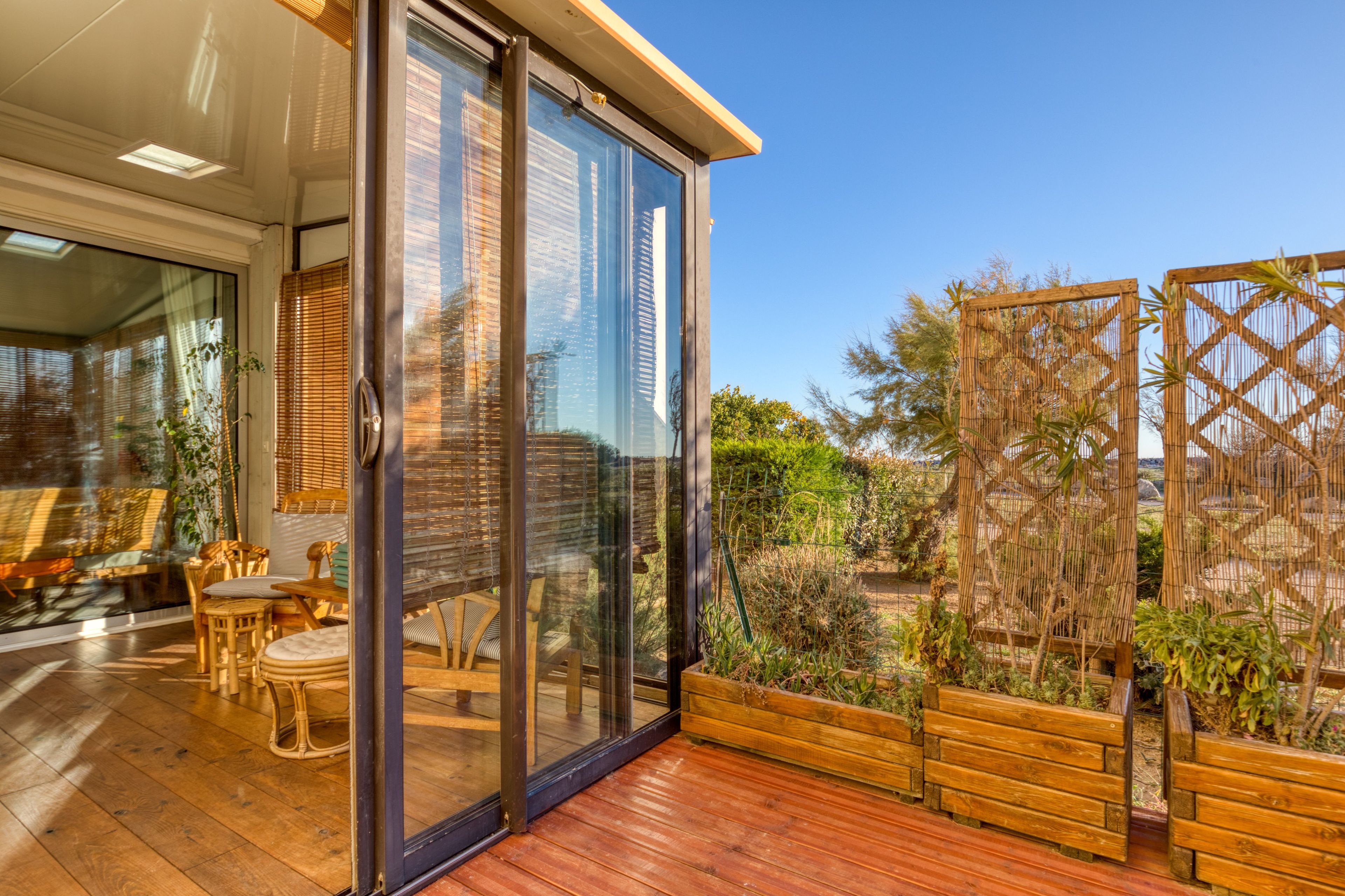 Eine moderne Terrassengestaltung mit Holzdeck, Glas-Schiebetüren und einer Sitzecke mit Korbmöbeln.