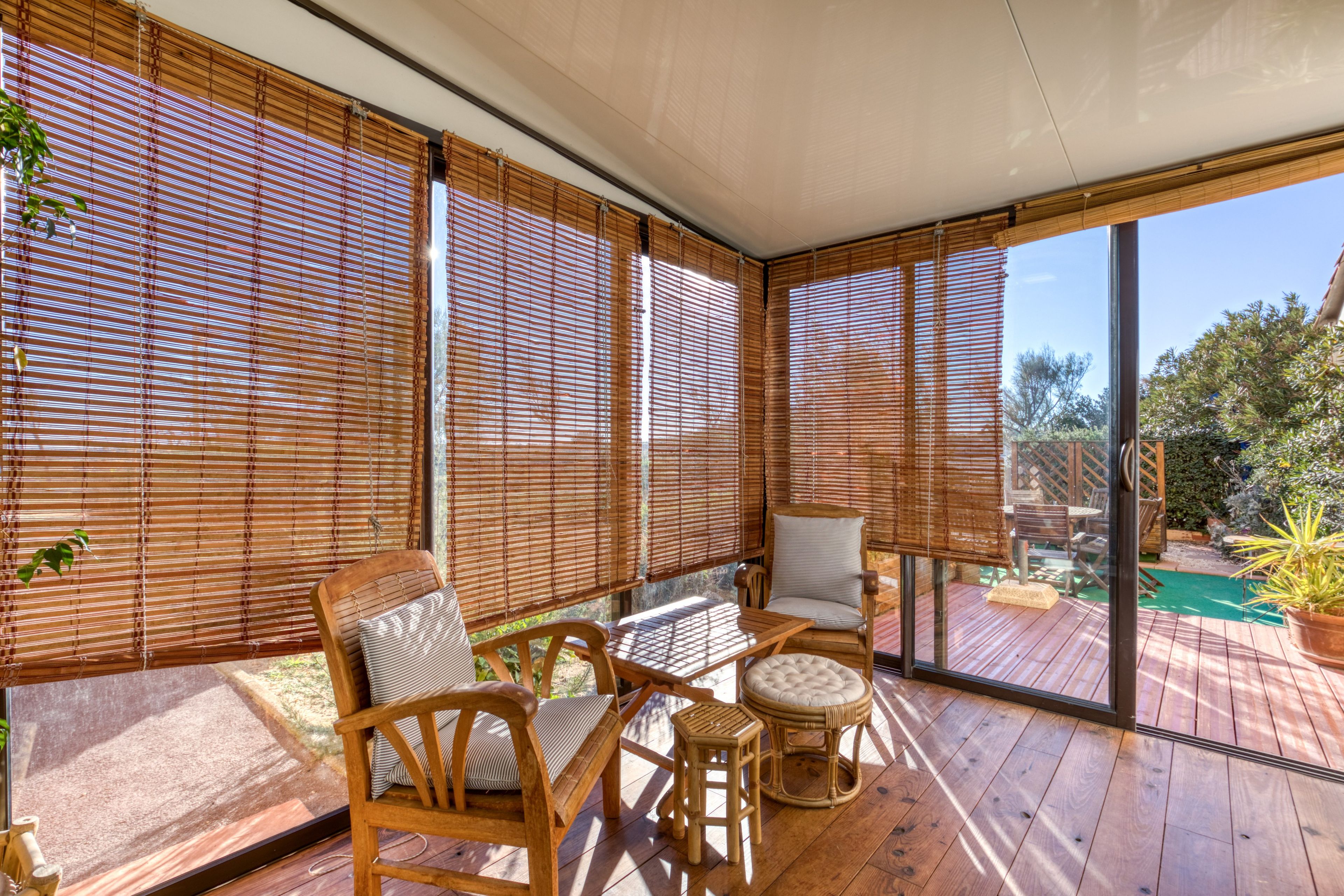 A covered outdoor seating area with wooden furniture and bamboo blinds.