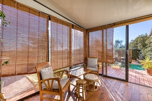 A covered outdoor seating area with wooden furniture and bamboo blinds.