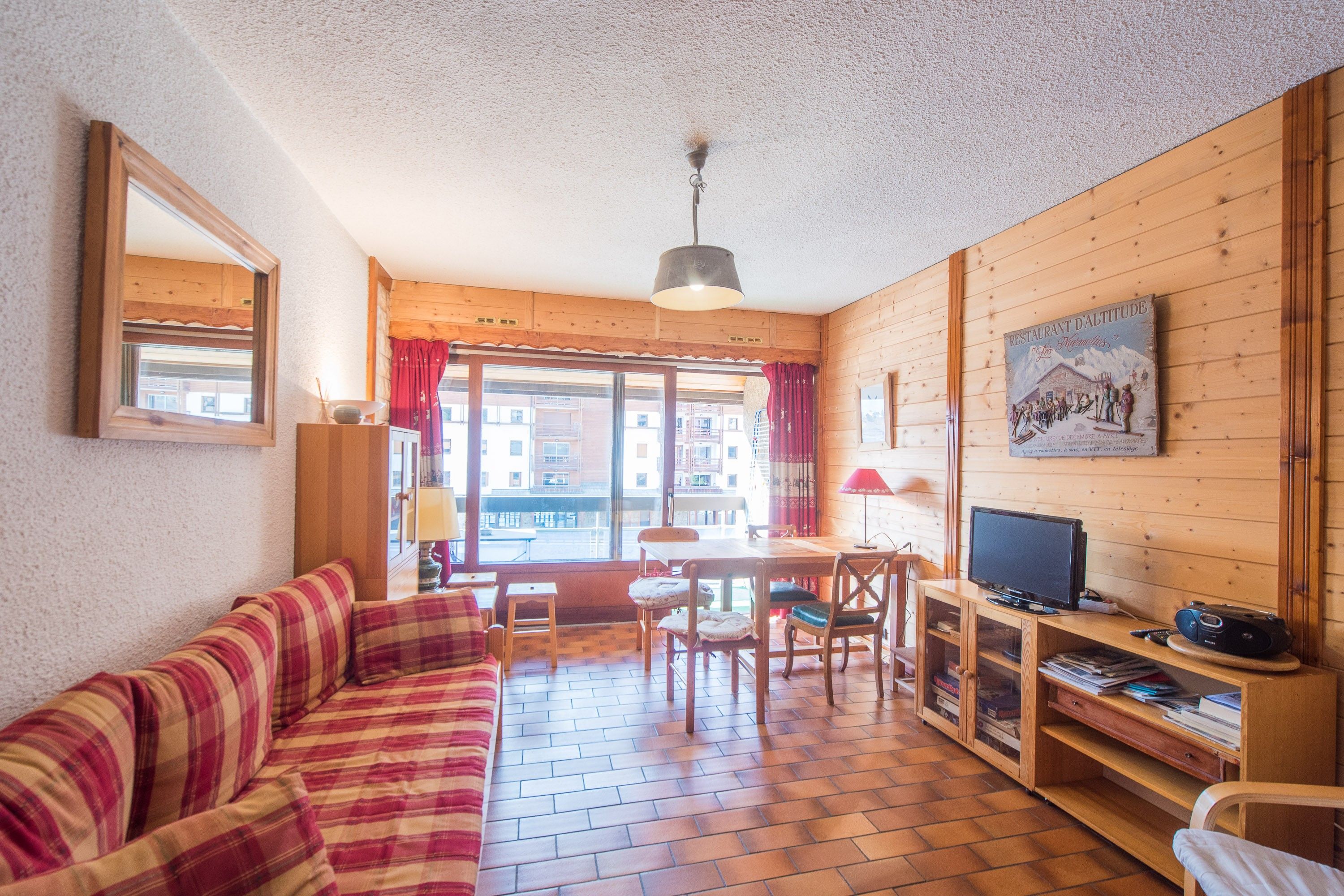 A cozy room with a wooden floor, a sofa, a dining table with chairs, a television, and a bookshelf.
