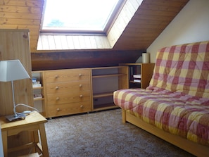 A bedroom with a sloped ceiling, a bed with a checkered bedspread, a wooden dresser with drawers, and a desk with a lamp. - Serre-Chevalier Vallée Briançon (Briançon)